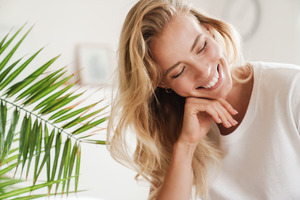 Woman in white shirt smiling and resting face on hand